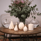Collection de bougies artisanales en cire naturelle, aux designs torsadés et géométriques, disposées sur une table en bois pour une ambiance cosy et raffinée. Fabriquée en Alsace
