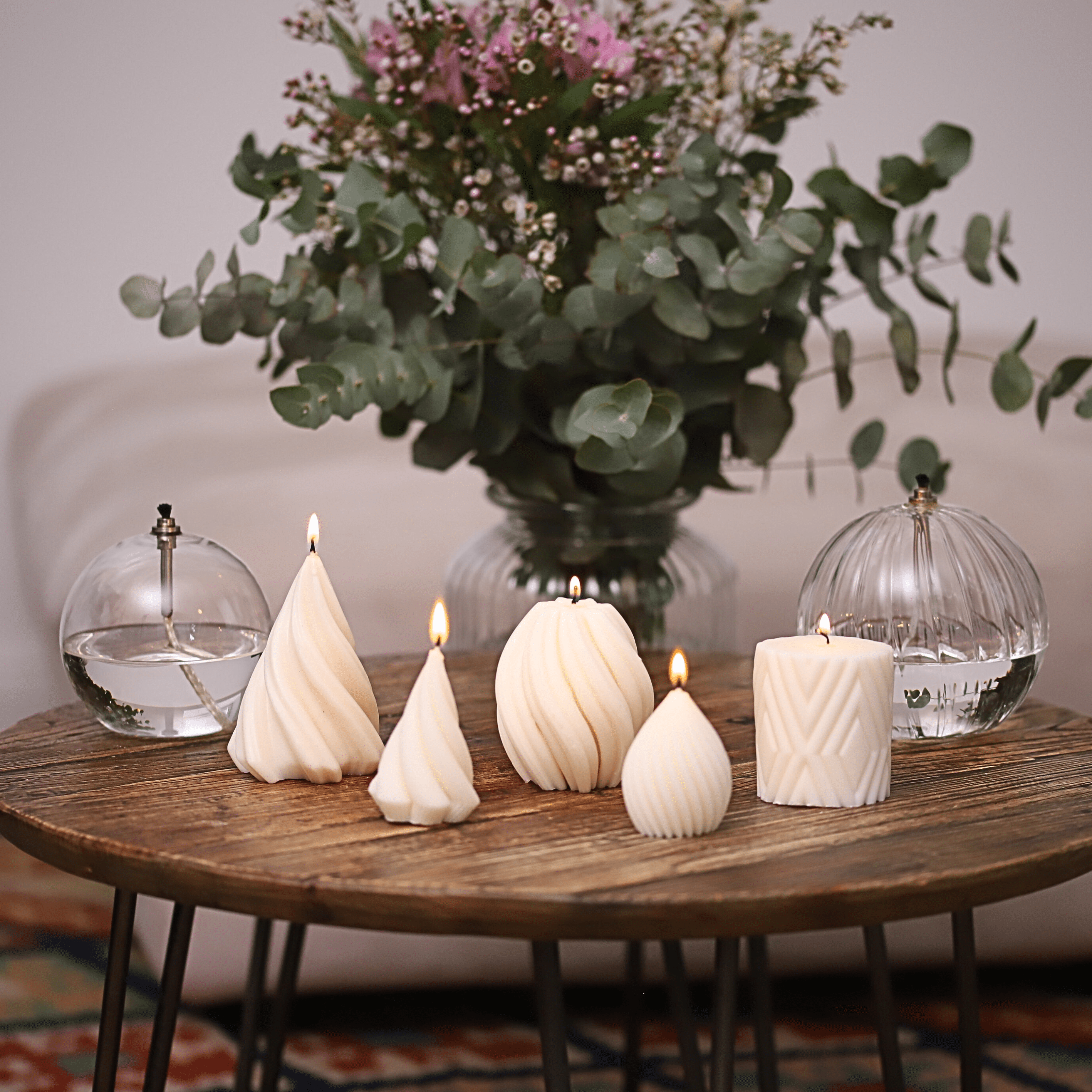 Collection de bougies artisanales en cire naturelle, aux designs torsadés et géométriques, disposées sur une table en bois pour une ambiance cosy et raffinée. Fabriquée en Alsace